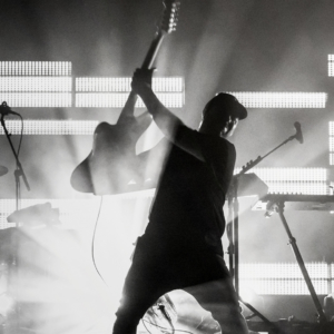 black and white image of martins silhouette raising the guitar in the air and jonny playing drums in the background