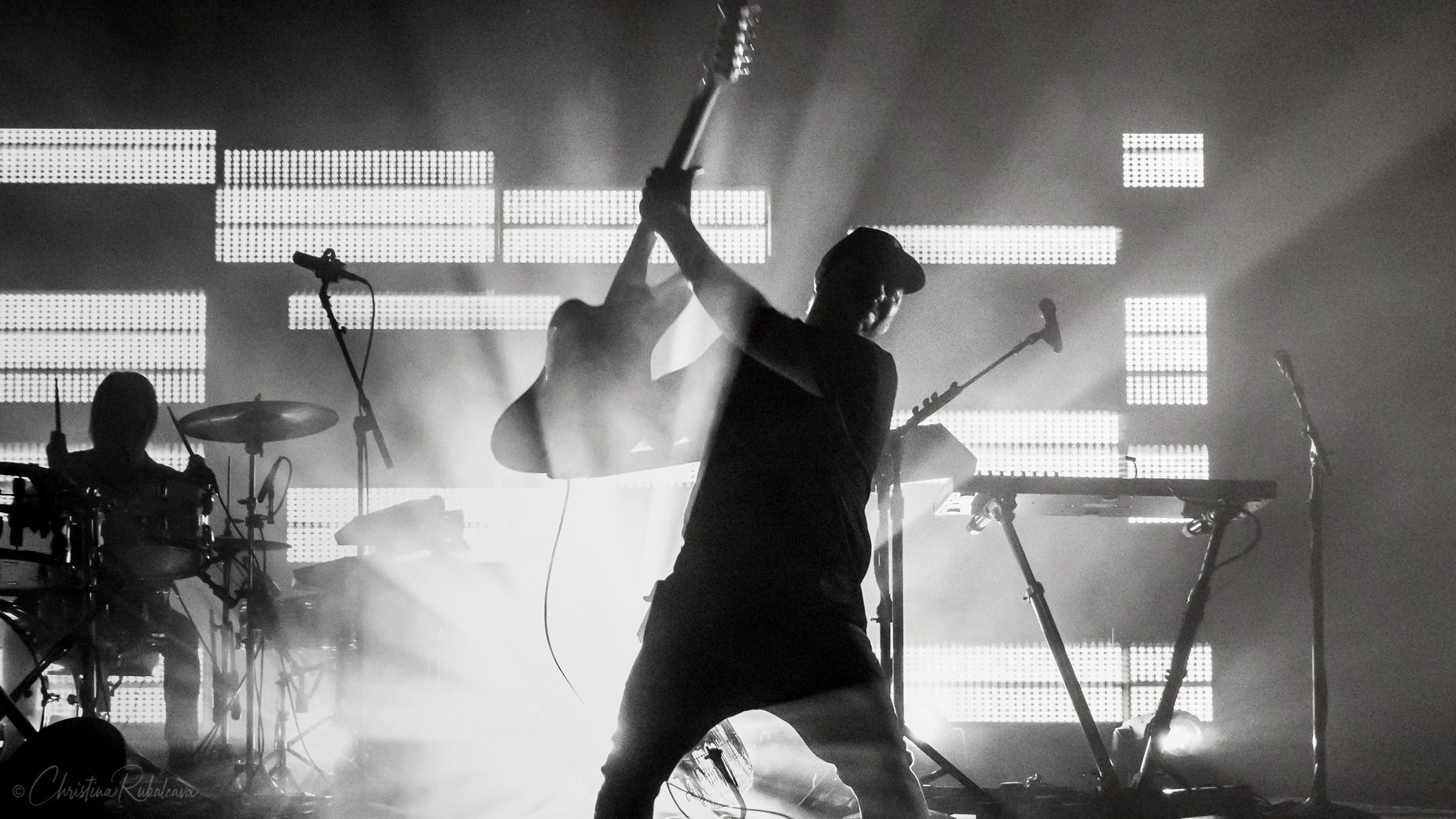 black and white image of martins silhouette raising the guitar in the air and jonny playing drums in the background