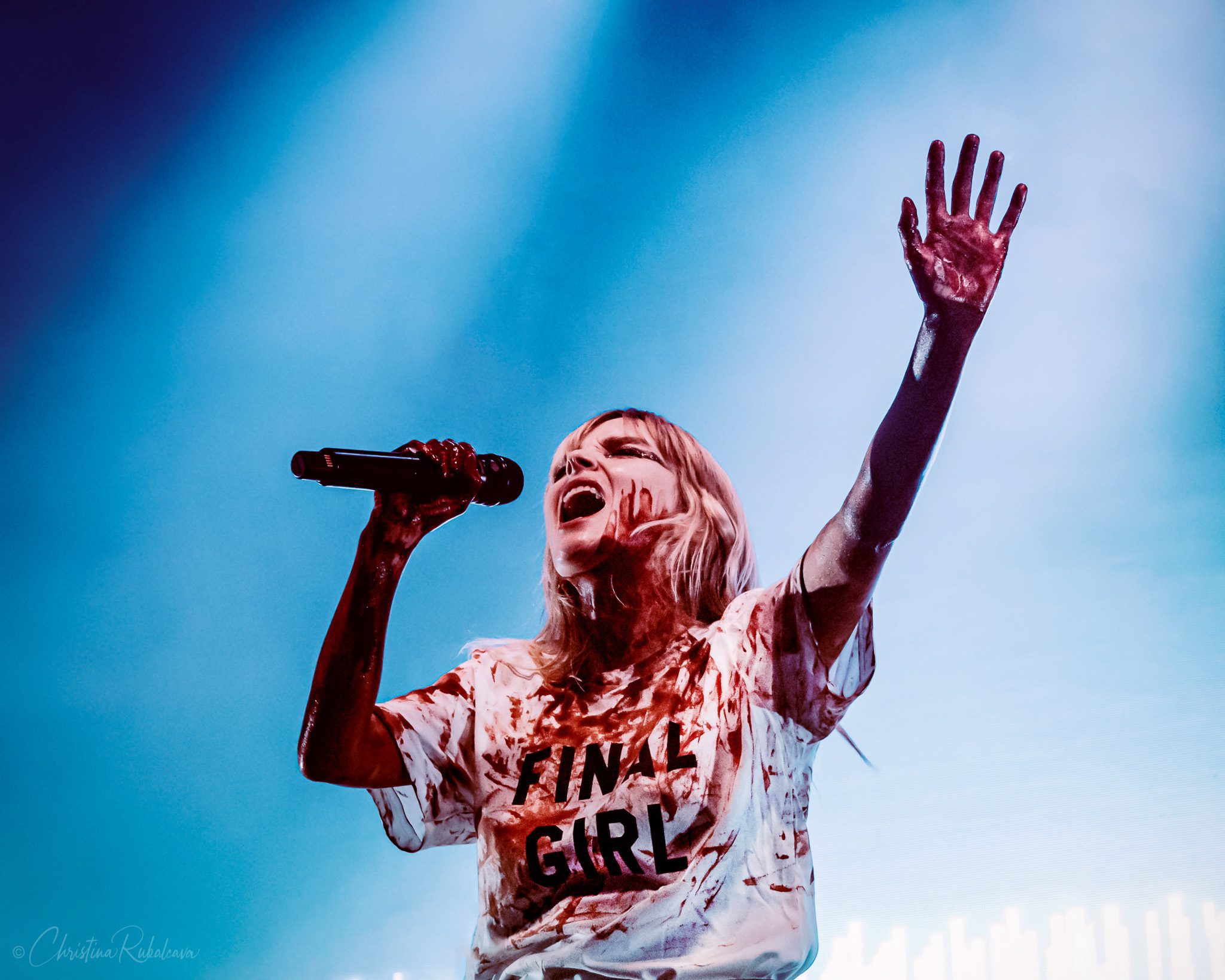 Lauren Mayberry singing into the microphone wearing a white T-shirt that says Final Girl on it and covered in fake blood.