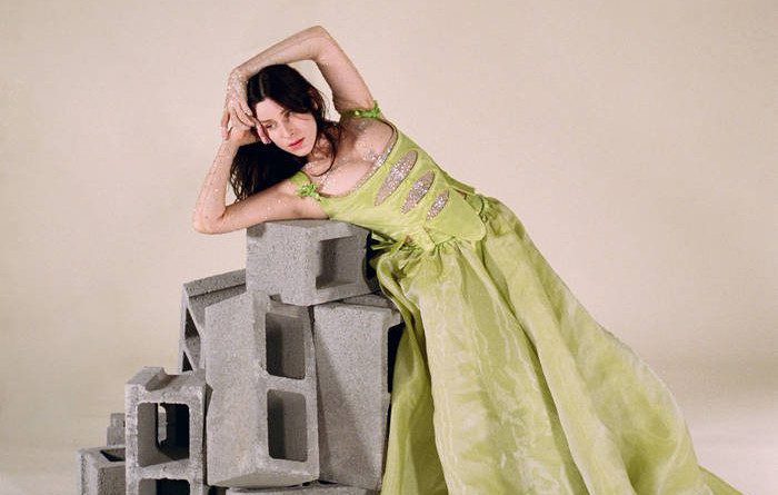 Sasha wearing a green dress sitting and leaning on a pile of cinderblocks