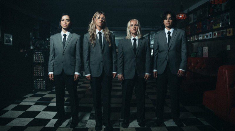 The Aces band members standing shoulder to shoulder wearing grey suits, white button up and black ties