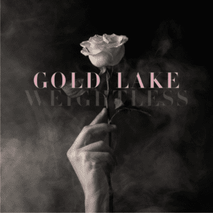 Cover image for Gold Lakes album "weightless" its a black and white image of a hand in the center, holding a single white rose. There is white smoke and font in a soft pink color with the name gold lake and the album name.