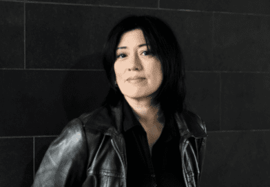 Miki Berenyi portrait. Miki is wearing a black leather moto style jacket, black top and is against a black background