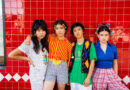 The band The Linda Lindas Standing in a row in front of a red tile wall